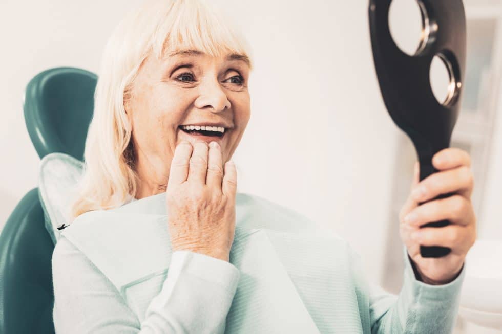 woman looking at her teeth in mirror while sitting in dental chair