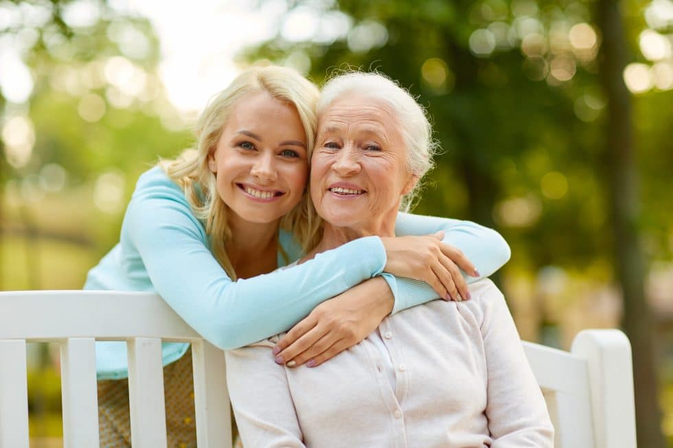 woman hugging senior woman sitting on bench