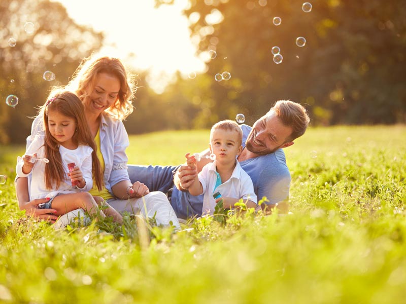 family of four blowing bubbles in grass